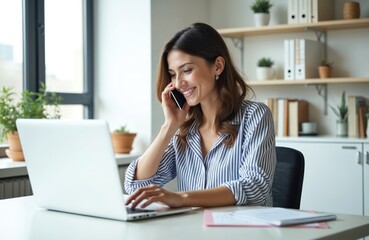 Obraz premium Attractive businesswoman works in modern office, speaks by phone. Smiling female manager uses laptop computer, checks business info. Happy entrepreneur consults client online, remote work.