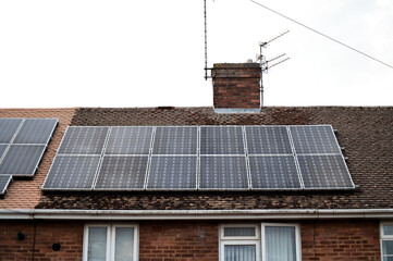 Wide view of solar panels mounted on the roof of a red brick house in a British residential area,...