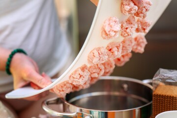 Girl's hands bending a plastic cutting board to release frozen chicken meatballs into a cooking pot