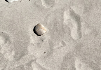 A single smooth, light-colored stone rests on a vast expanse of fine, light-colored sand, creating a minimalist and serene natural background.