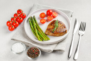 Close up, macro of tasty grilled beef steak served with green asparagus and cherry tomatoes on white plate, with cutlery. Perfect for food menu, diet, or culinary design concepts.