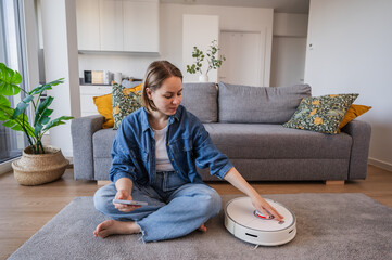 Woman turns on smart vacuum cleaner to clean up the house. Smart home concept