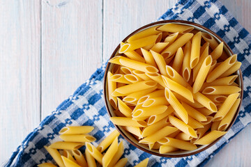 Penne Pasta in Bowl on Blue White Kitchen Towel Wooden Background