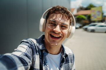 Young adult man student smile with wireless headphones take self portrait or video call