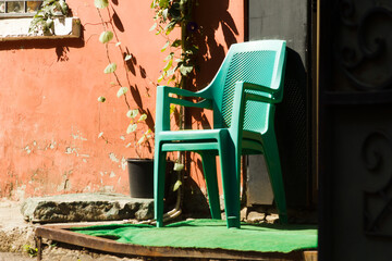 Urban street scene with two green plastic chairs stacked near a red weathered wall in bright...