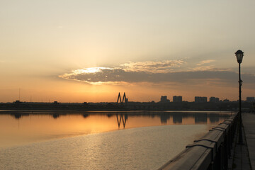 Serene sunset over a calm river with reflections of a modern cable-stayed bridge and distant city...