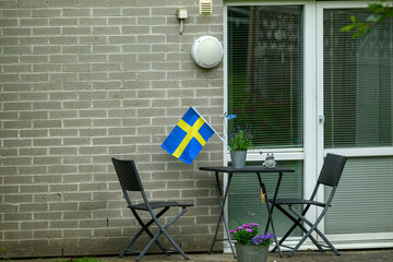 A small outdoor area features a Swedish flag hanging next to a round table and two chairs. Colorful...