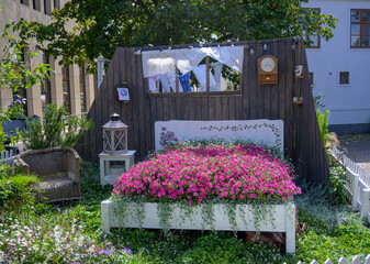 A unique outdoor garden showcases a bed frame filled with blooming pink flowers. Decorative items...