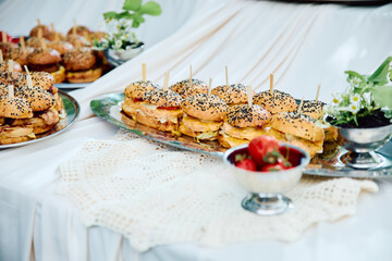 Outdoor buffet with assorted mini sandwiches on silver platter, garnished with herbs and...