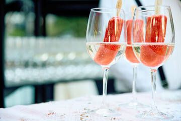 Elegant outdoor scene with three glasses of sparkling water infused with fresh strawberry slices,...