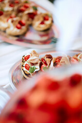 Close-up of strawberry-topped mini tarts with garnished basil leaves, arranged on a silver tray...