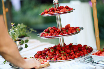 Outdoor three-tiered silver tray overflowing with ripe strawberries, surrounded by spring flowers...