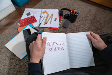 Hands using red stencil to draw letters on notebook with school supplies scattered around