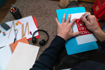 Student using stencil and studying on floor at home surrounded by school supplies