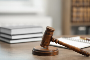 Judge's gavel, books and notebook on wooden table in office, closeup