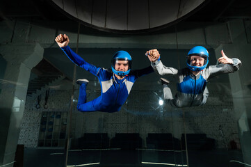 A male instructor teaches a woman how to fly in a wind tunnel. Free fall simulator.