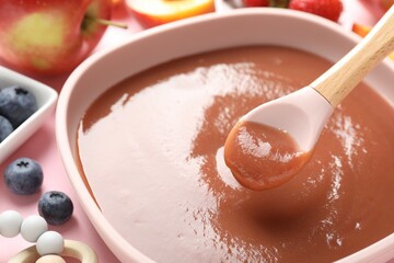Baby food. Eating tasty puree with spoon at pink table, closeup