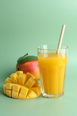 Tasty mango juice in glass and fresh fruits on green background