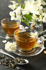 Aromatic jasmine tea, brew and flowers on grey table, closeup