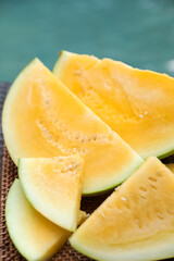 Pieces of ripe yellow watermelon on wicker table near swimming pool, closeup