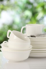 Different clean dishes on white table against blurred green background, closeup