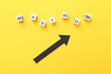Word Maximum made of beads with letters and arrow pointing at it on yellow background, flat lay