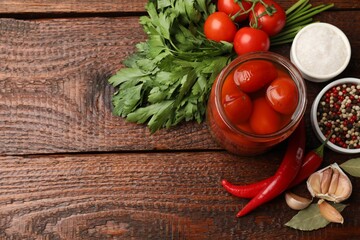 Tasty pickled tomatoes in jar and ingredients on wooden table, flat lay. Space for text