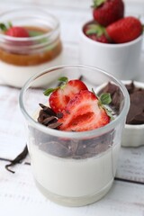 Tasty panna cotta with chocolate, strawberries and vanilla on white wooden table, closeup