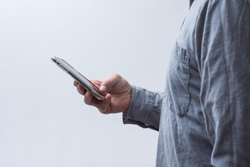Man in shirt holding smartphone on light background. Portable mobile technology concept.