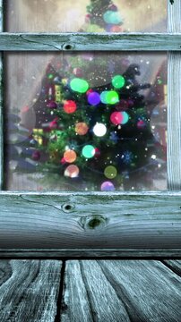 Animation of wooden window frame with snow falling over christmas tree and cottages outside