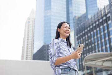 close up manager businesswoman hold smartphone and looking away through while stand outside office building tower for better vision and thinking about new business project for startup