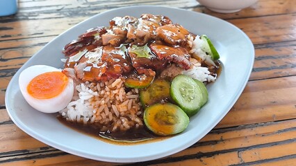 Red pork and crispy pork on rice in a blue plate on a wooden  table in Thailand
