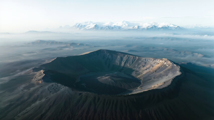 Breathtaking Aerial View of Volcanic Crater with Distant Snowy Mountains and Mist