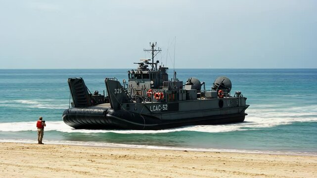 A landing craft air cushion approaches the beach with a person in uniform standing on the sand