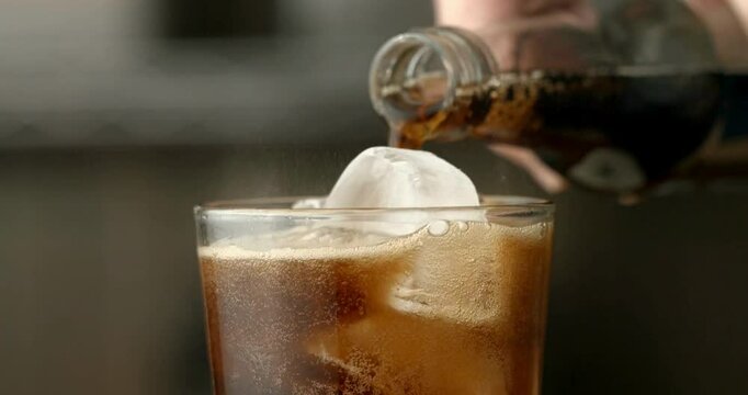 Close-up video of a glass with ice being filled with soda
