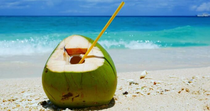 Video of a coconut with a straw on the beach. The background has a blurred effect.