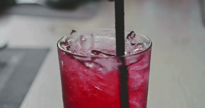 Close-up video of a glass of hibiscus tea being swirled with a straw and ice cubes. High quality with a blurred background.