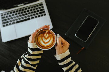 A cozy moment of balance and focus as a person enjoys a latte, checks their smartphone, and works...