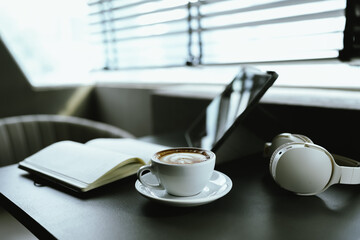Young Asian woman making latte in a relaxed atmosphere with laptop and notebook and notepad while combining work and relaxation during a quiet coffee break at home or office.
