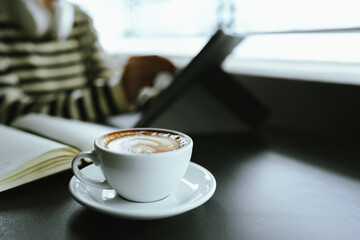 Young Asian woman making latte in a relaxed atmosphere with laptop and notebook and notepad while combining work and relaxation during a quiet coffee break at home or office.