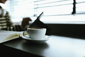 Young Asian woman making latte in a relaxed atmosphere with laptop and notebook and notepad while combining work and relaxation during a quiet coffee break at home or office.