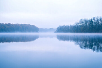 Misty Morning Landscape Over Calm Water with Reflections