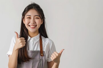 Happy Young Asian Barista Female Staff Worker in Apron Showing Thumbs Up and Pointing at Copy Space