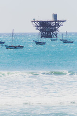 A group of small boats are floating in the ocean near a large oil rig
