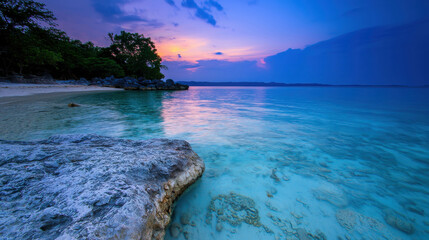 Obraz premium Serene coastal landscape with turquoise water, rocky foreground, vibrant sunset, tropical island atmosphere, and lush greenery near calm ocean waves