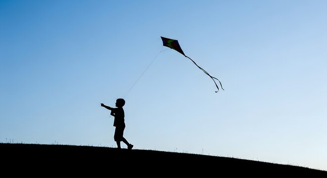 Silhouette of a boy flying a colorful kite on a grassy hill against a clear sky - Powered by Adobe