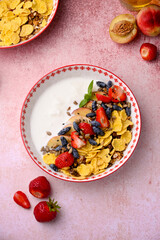 Plate with yogurt and muesli topped with fresh strawberries on pink background. Summer breakfast...