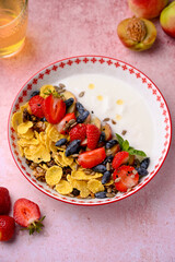 Plate with yogurt and muesli topped with fresh strawberries on pink background. Summer breakfast...