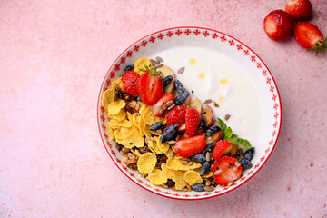 Plate with yogurt and muesli topped with fresh strawberries on pink background. Summer breakfast concept, light and refreshing morning meal.