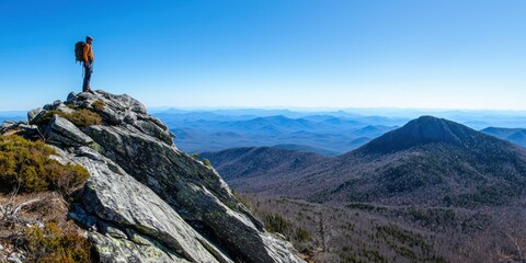 A hiker standing on a rocky peak, overlooking layers of mountain ridges